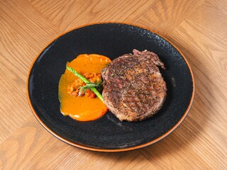 Grilled ribeye steak with sweet pepper sauce and asparagus on black ceramic plate