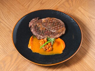 Grilled ribeye steak with sweet pepper sauce and asparagus on black ceramic plate