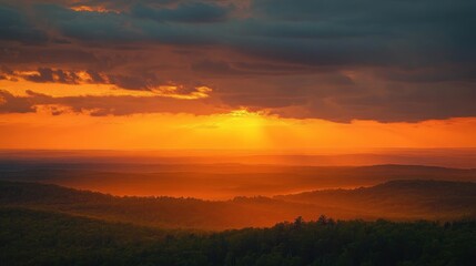 Obraz premium Vibrant sunset casting golden light over layered forested hills under dramatic dark clouds