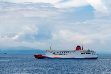 Passenger ferry sailing across calm blue sea with a mountainous coastline in the background under a...