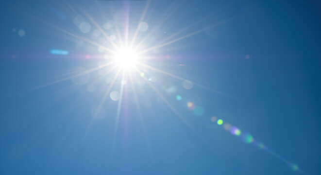 Bright sun with radiating rays against clear deep blue sky with lens flare effect. Natural summer phenomenon creates warm atmosphere for seasonal promotions and outdoor activities