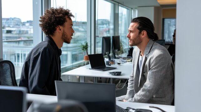 Two Business Professionals Engaging in Discussion at Modern Office Space with Large Windows and Natural Light