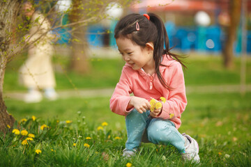 Happy Little Girl Picking Dandelions in Spring Park