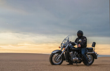Man on motorcycle in desert during sunset with dramatic clouds — concept of freedom, travel, solitude, adventure, and outdoor lifestyle in wild open landscapes