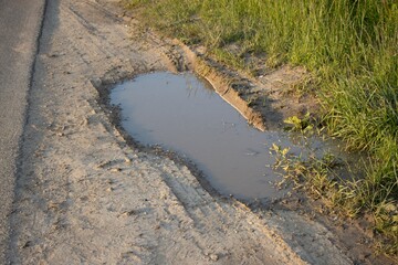 A puddle near the asphalt road in the light of the setting sun.