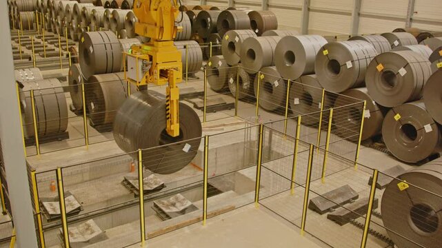A crane putting down a large and heavy steel coil in a large factory