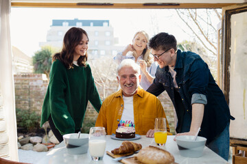 Family celebrating a senior man's birthday at home with a cake and breakfast
