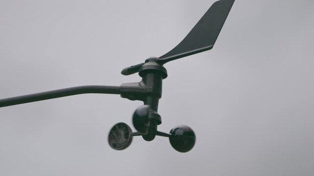 Close up, An Anemometer spinning and turning in the breeze with a grey and cloudy sky background.