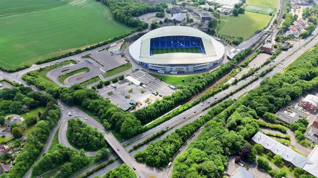 Slow aerial drift reveals Brighton&rsquo;s stadium nestled below, cradled by a web of trains and a humming motorway. A serene approach to a pulse of energy.