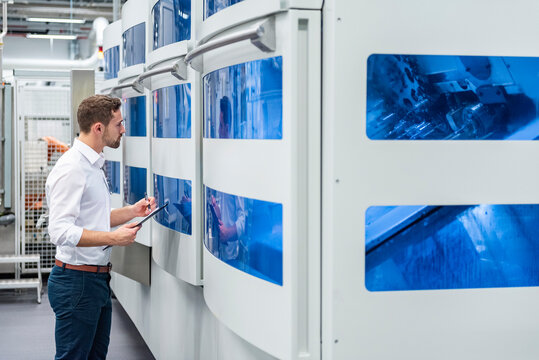 Employee inspecting machines in a production hall with a clipboard