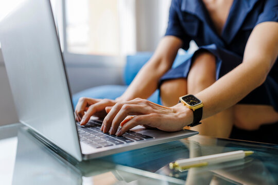 Unrecognizable person typing on a laptop at a glass table in a home office