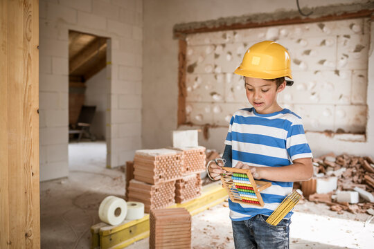 Boy wearing hardhat counting bead of abacus while standing at loft