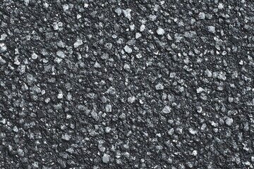 A detailed, textured shot of asphalt, showcasing its rough, gritty surface. The image captures the fine details of the road material