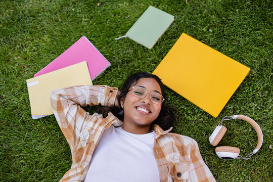 Student relaxing on grass with study materials and headphones outdoors