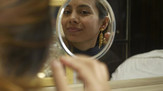 Young beautiful asian woman looking at mirror wearing 18k HUID certified gold earrings