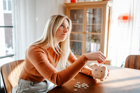 Woman looking sad while holding a piggy bank and coins indoors