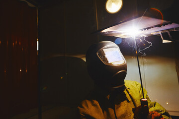 Worker in safety mask welds metal at industrial enterprises.
