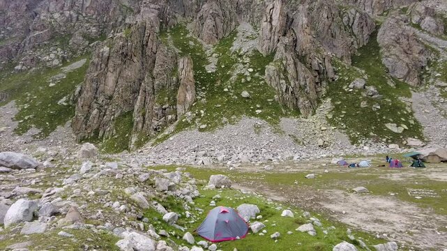 Mountain basecamp with tents set on rocky alpine plateau surrounded by steep cliffs and patches of greenery. Concept of high-altitude hiking expedition