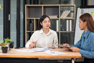 Group of happy Asian business people having a meeting at the office. Two women working together using modern laptops.