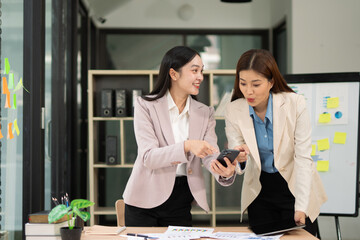 Two excited Asian businesswomen raising their arms and delighted at a successful company event in an office environment.