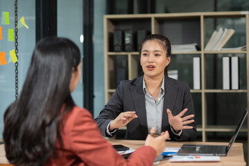 Two professional business executives working on laptop computer sitting at office desk, happy colleagues discussing company digital strategy.
