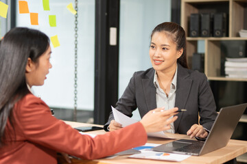 Two professional business executives working on laptop computer sitting at office desk, happy colleagues discussing company digital strategy.