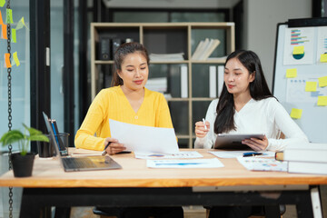 Obraz premium Two professional business executives working on laptop computer sitting at office desk, happy colleagues discussing company digital strategy.