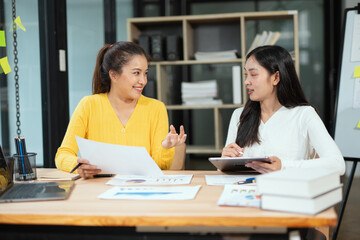 Two professional business executives working on laptop computer sitting at office desk, happy colleagues discussing company digital strategy.