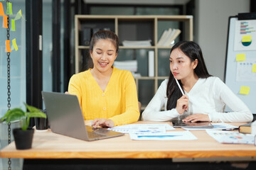 Obraz premium Two professional business executives working on laptop computer sitting at office desk, happy colleagues discussing company digital strategy.
