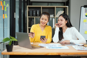 Two professional business executives working on laptop computer sitting at office desk, happy colleagues discussing company digital strategy.