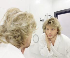 Fototapeta premium morning routine, young man looking in mirror in bathroom