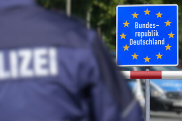 Ein Polizist steht an der deutschen Grenze vor dem Schild Bundesrepublik Deutschland