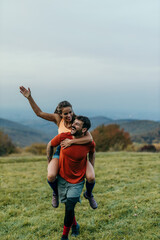 Fototapeta premium Happy couple piggybacking in a meadow with mountain view: celebrating successful hike