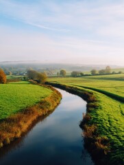 Serene river winding through lush green fields under a clear sky at dawn, peaceful countryside
