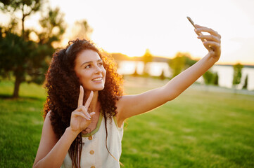 woman taking selfie with smartphone outdoors. energetic young woman capturing moment at sunset in...