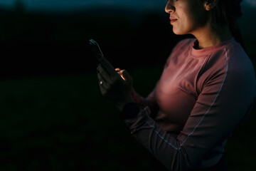 Sportswoman using smartphone in the dark after sunset