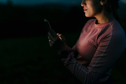 Sportswoman using smartphone in the dark after sunset - Powered by Adobe