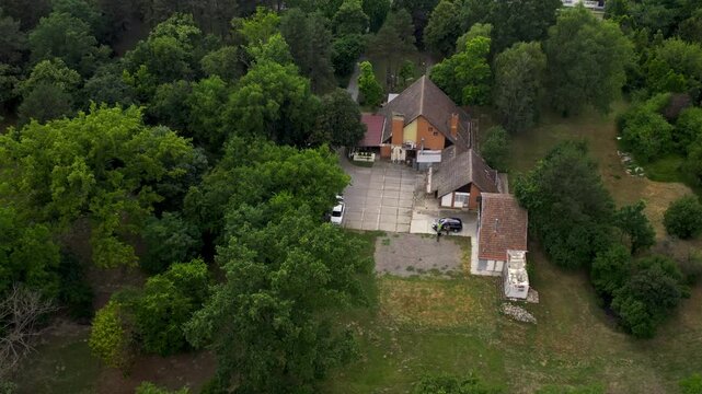 Explore Becej's serene landscape featuring an inviting lodge nestled among lush greenery on a tranquil day
