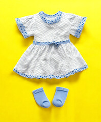 Adorable baby girl outfit including a polka dot dress with blue floral trim and socks on yellow backdrop