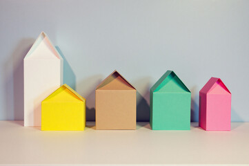Row of colorful paper houses sitting on top of a white table against a wall in background.