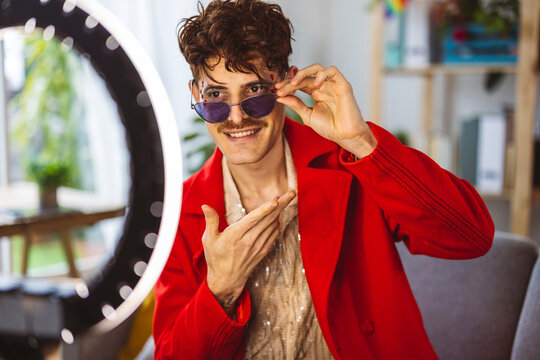 Happy influencer wearing sunglasses and gesturing in front of ring light at home