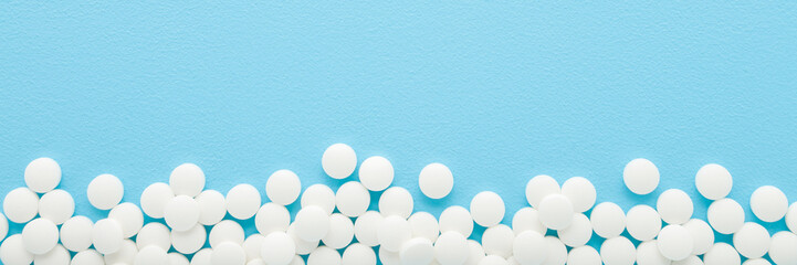 White pills on light blue table background. Pastel color. Closeup. Wide banner. Empty place for text. Top view. Top down view.