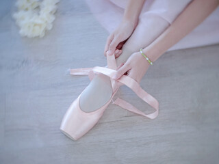 A womans hands tying ballet slippers. Pastel and white tones © wisannumkarng