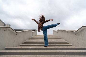 Ballerina dancing, low-angle view, on concrete stairs under a cloudy sky