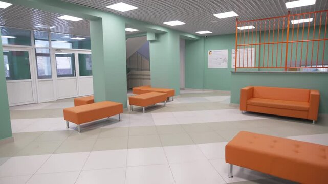 Vivid sofas stand in quiet lobby while light columns divide space. Registration window appears closed and hallway remains empty and tidy