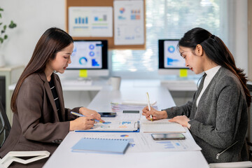 Two women are sitting at a desk, writing on paper