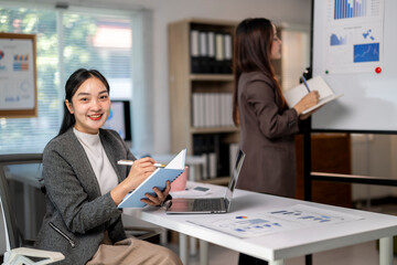 A woman is sitting at a desk with a laptop and a notebook