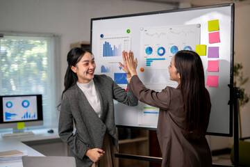 Two women are high fiving each other in front of a white board with graphs