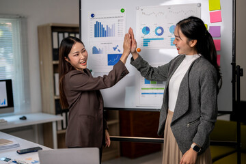 Two women are high fiving each other in front of a white board with graphs on it