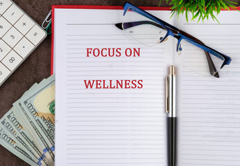 A notebook open with the words focus on wellness featured prominently. Nearby are reading glasses,...